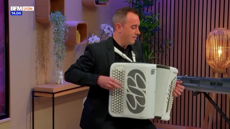 A man in a black suit sits playing a white accordion, his fingers dancing across the keys. The BFM Lyon logo is visible in the corner, suggesting a live performance is underway.
