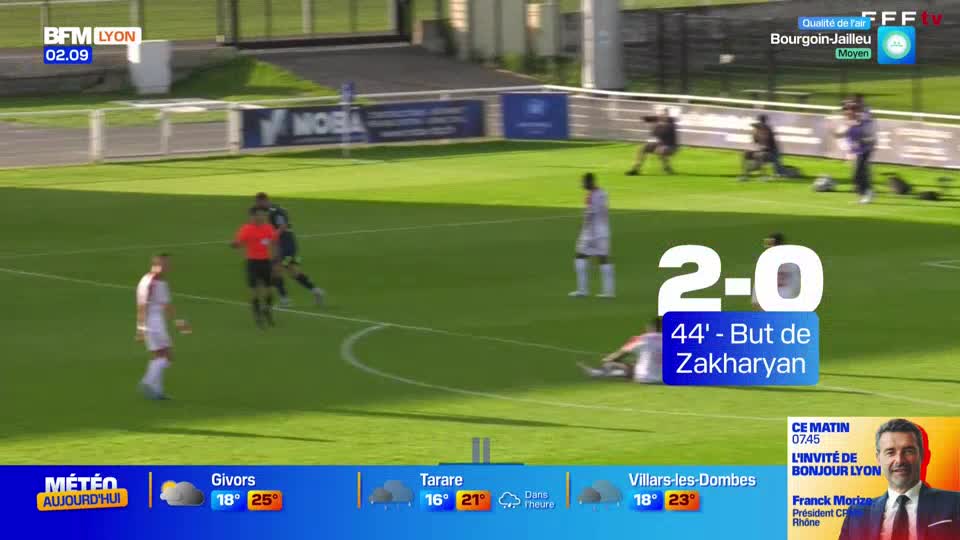 A player in white is sprawled on the grass after a goal, while the referee in orange jogs toward the action. The scoreboard shows the score is 2-0 in the 44th minute, with Zakharyan having scored.
