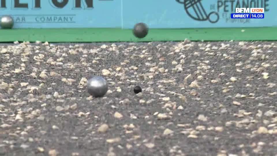 A steel ball is suspended mid-air, while another rolls across the gravelly ground. The small black jack sits still, waiting for the next shot.
