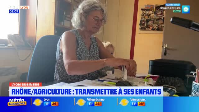 A woman with gray hair sits at a desk, intently working with papers. Behind her, a child peeks over her shoulder, as the BFM Lyon news segment focuses on Rhone/Agriculture.
