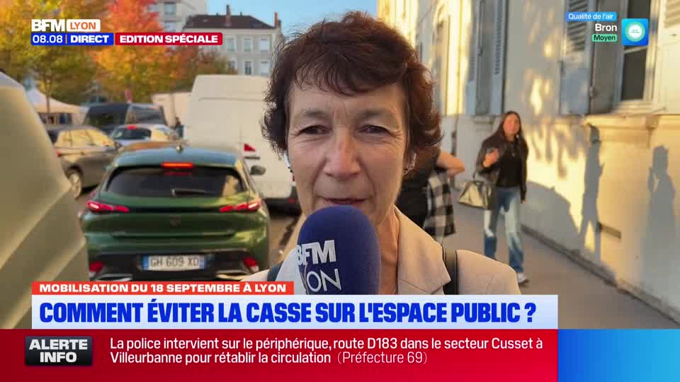 A woman in a beige jacket speaks into a BFM Lyon microphone, with a green car and other vehicles visible behind her. The news broadcast is reporting on a demonstration in Lyon and how to avoid damage to public space.
