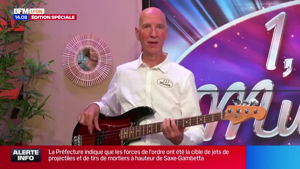 A man in a white shirt holds a bass guitar, looking directly at the camera. The BFM Lyon logo is visible, and the news ticker below reports on a police situation in France.
