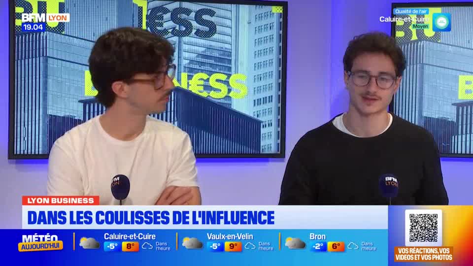 Two men with glasses are seated at a desk, microphones in front of them, on the BFM Lyon set. The man on the right is speaking, while the other looks on, both framed by a backdrop of a building.
