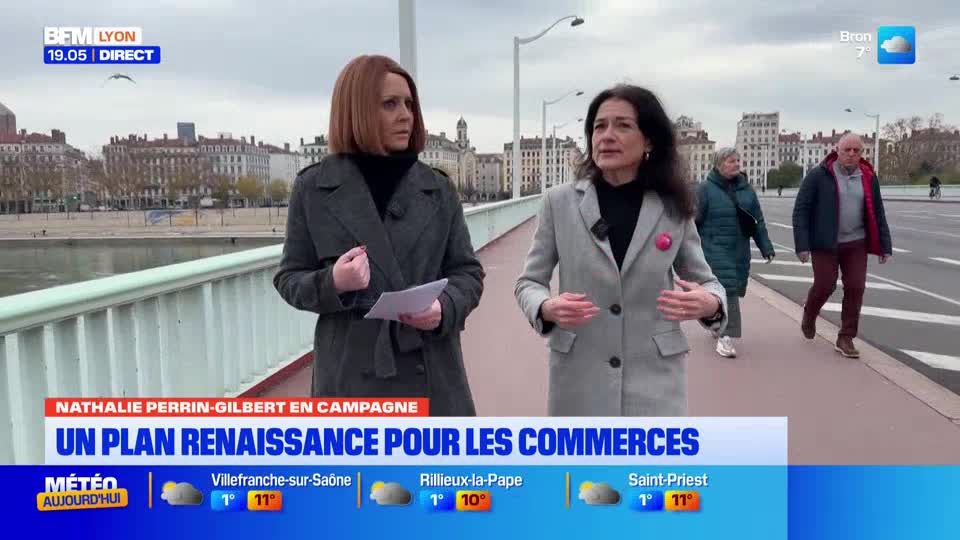 On a bridge in Lyon, two women stand facing the camera, speaking. Behind them, a couple walks along the sidewalk, and the city stretches out in the background.
