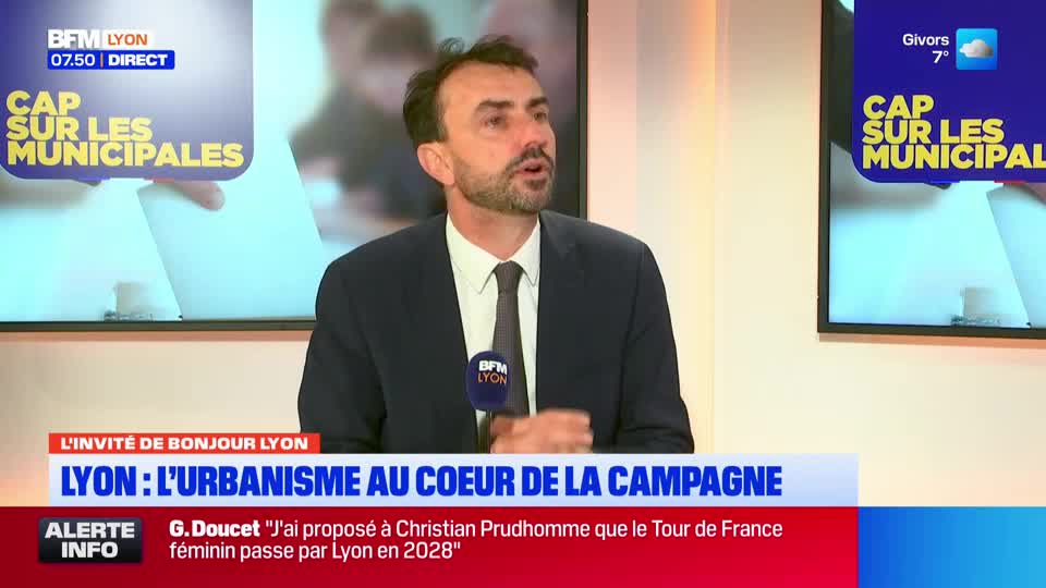 A man in a suit speaks into a microphone on a BFM Lyon broadcast. On screens behind him, graphics display "Cap sur les Municipales" and weather information for Givors. A man in a suit speaks into a microphone on a BFM Lyon broadcast. On screens behind him, graphics display "Cap sur les Municipales" and weather information for Givors.