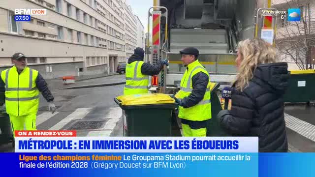Two sanitation workers in bright yellow vests are collecting trash bins in Lyon. A reporter stands nearby, holding a microphone with the BFM Lyon logo. Two sanitation workers in bright yellow vests are collecting trash bins in Lyon. A reporter stands nearby, holding a microphone with the BFM Lyon logo.