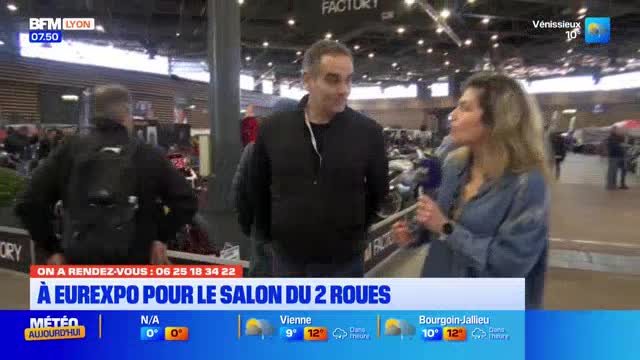 A reporter interviews a man at the Salon du 2 Roues in Eurexpo, Lyon. Behind them, people mill around displays of motorcycles. A reporter interviews a man at the Salon du 2 Roues in Eurexpo, Lyon. Behind them, people mill around displays of motorcycles.