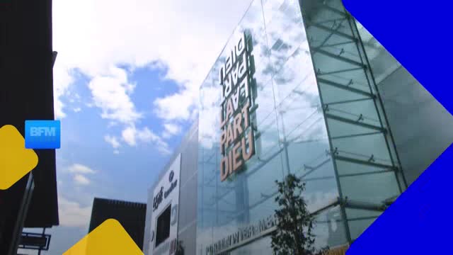 A modern glass building stands tall against a bright sky, its facade reflecting the clouds. The BFM Lyon logo is visible on a blue square in the foreground. A modern glass building stands tall against a bright sky, its facade reflecting the clouds. The BFM Lyon logo is visible on a blue square in the foreground.