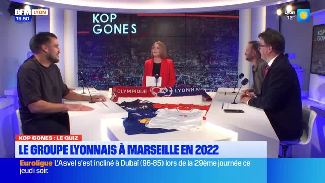 Four people sit at a desk in a television studio, with a screen behind them displaying "KOP GONES." A red blazer-clad woman stands behind a microphone, while three men are seated. In front of them, a Lyon scarf and several team jerseys are laid out. Four people sit at a desk in a television studio, with a screen behind them displaying "KOP GONES." A red blazer-clad woman stands behind a microphone, while three men are seated. In front of them, a Lyon scarf and several team jerseys are laid out.