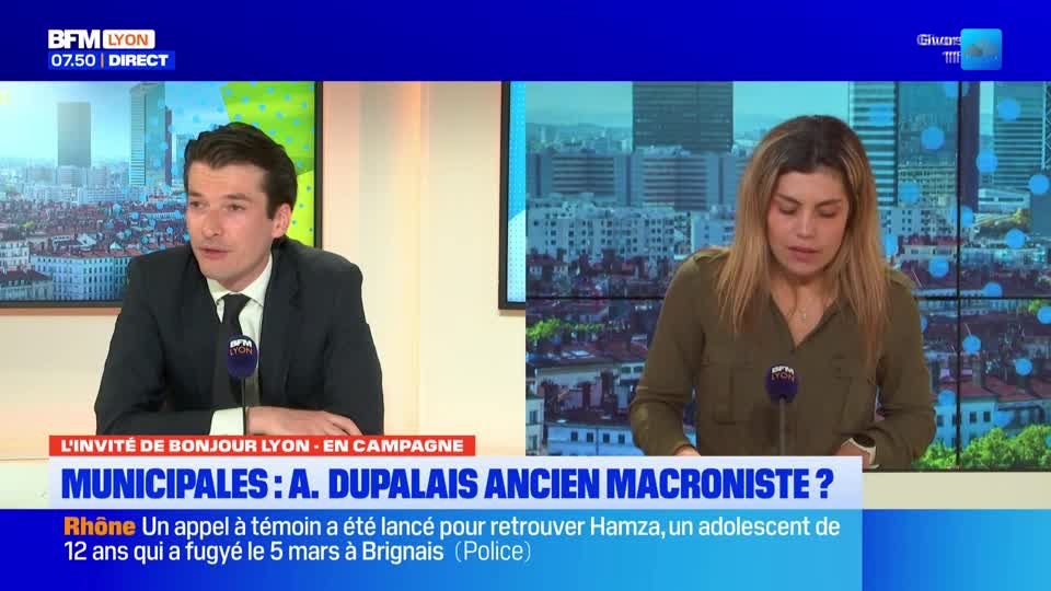 A man in a suit speaks into a microphone, while a woman in a green shirt looks down. Both are seated at desks in front of screens displaying cityscapes, with BFM Lyon branding visible.