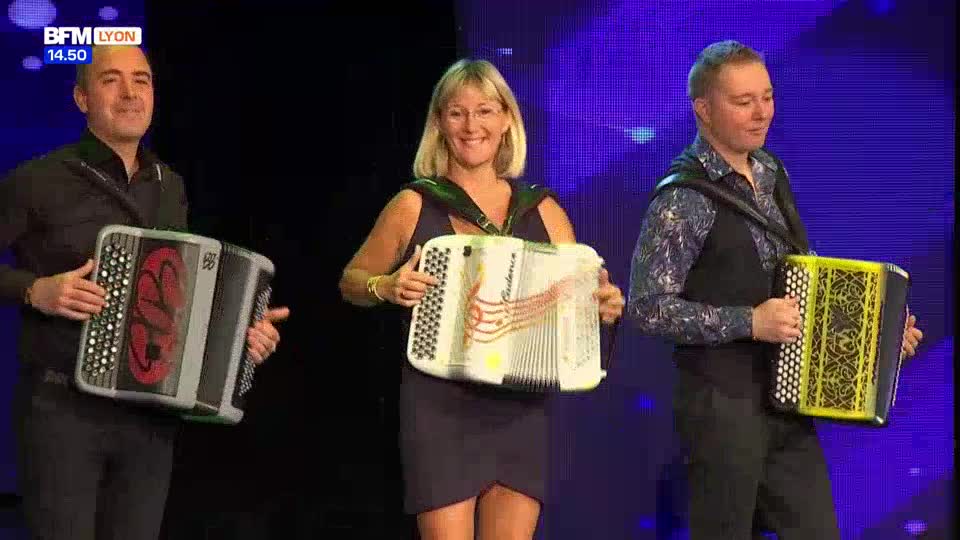 Three musicians stand on a stage, each holding an accordion. The BFM Lyon broadcast is visible in the upper left corner, indicating this is a French television segment.