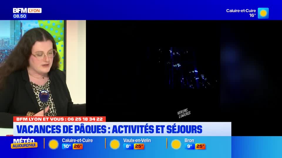 A woman in glasses speaks into a microphone, her dark hair framing her face. On the screen behind her, a dark landscape is illuminated by scattered blue lights. A woman in glasses speaks into a microphone, her dark hair framing her face. On the screen behind her, a dark landscape is illuminated by scattered blue lights.