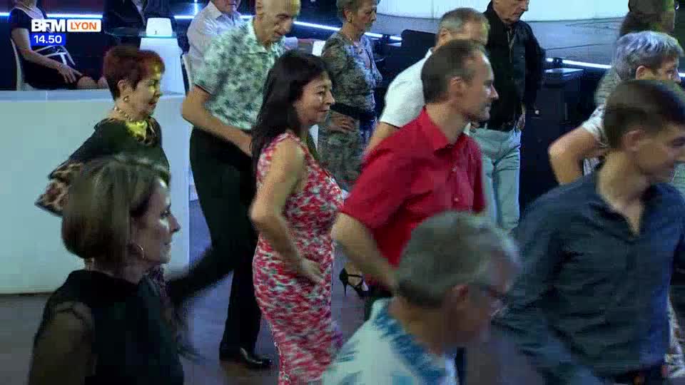 People are dancing in a room, their movements creating a gentle sway. A woman in a red and white floral dress moves with a smile, her hand on her hip. People are dancing in a room, their movements creating a gentle sway. A woman in a red and white floral dress moves with a smile, her hand on her hip.