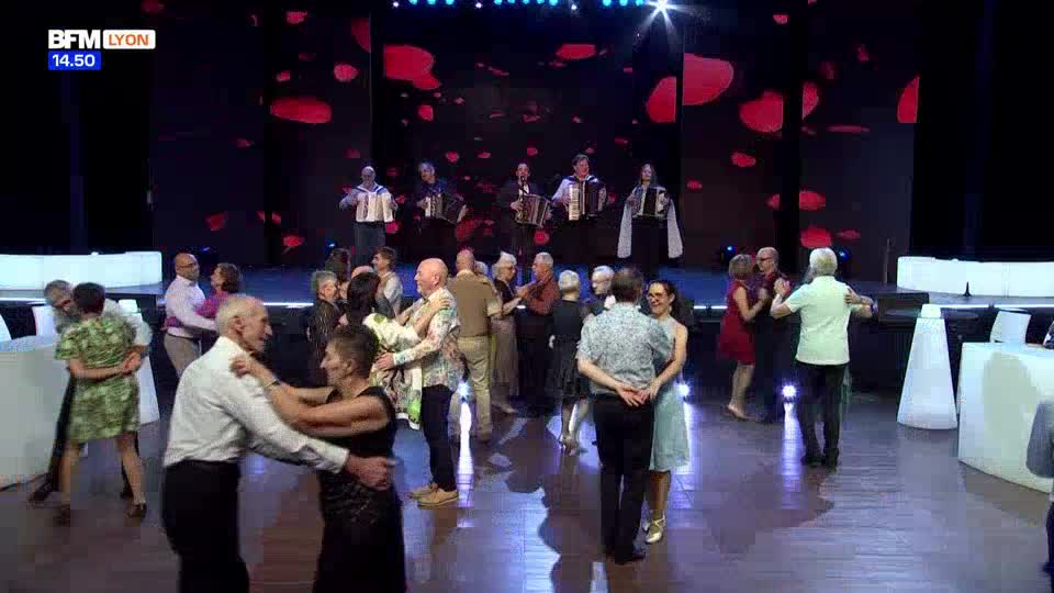 A group of accordionists plays on a stage while couples dance on the floor below. The BFM Lyon broadcast shows a lively scene of people enjoying themselves.