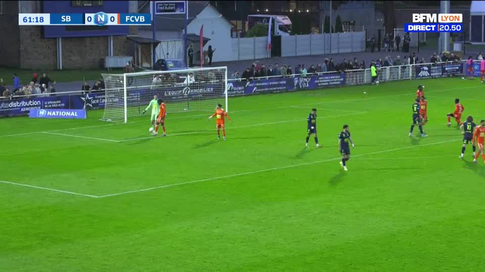 A player in an orange kit dribbles the ball towards the goal, defended by a goalkeeper in the same color. Other players in dark blue uniforms position themselves on the field, anticipating the play. The scoreboard shows the match is in its 61st minute with a 0-0 score.