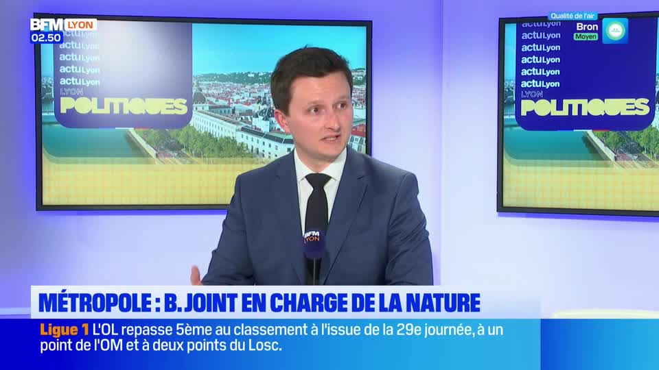 A man in a suit speaks into a microphone on a BFM Lyon set. Behind him, a screen displays "POLITIQUES" and a cityscape.