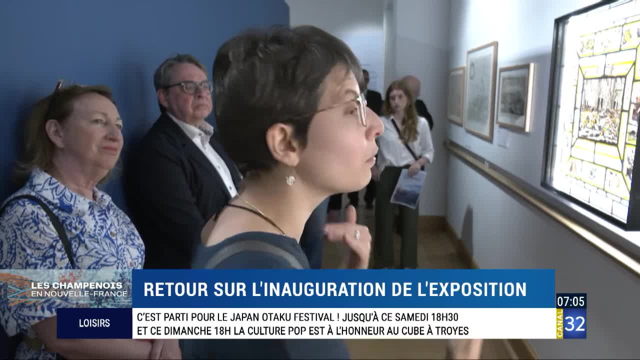 People are gathered in a gallery, looking at artwork. A woman in glasses studies a framed piece, while a news graphic from Canal 32 reports on an exhibition in France.
