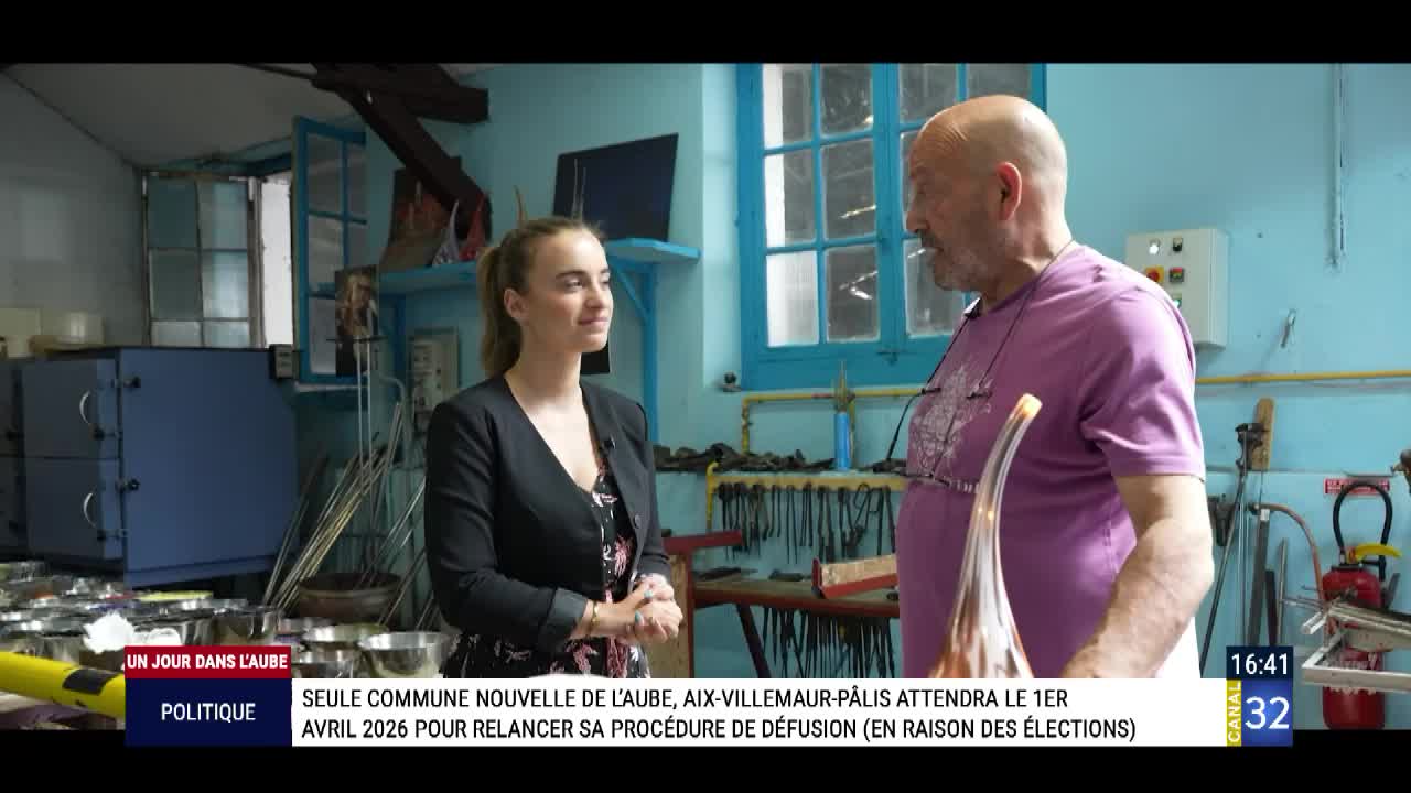 The woman in the black jacket is listening intently as the man in the purple shirt holds up a long, slender glass object. It looks like a segment from a Canal 32 segment, "Un jour dans l'Aube," with a political story about elections in the background.

