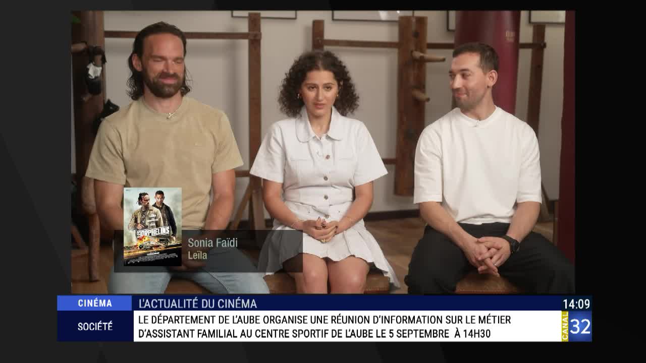 Three people sit on a set, with a movie poster visible beside one of them. The screen displays a Canal 32 graphic, and the bottom banner mentions a meeting in Aube, France.
