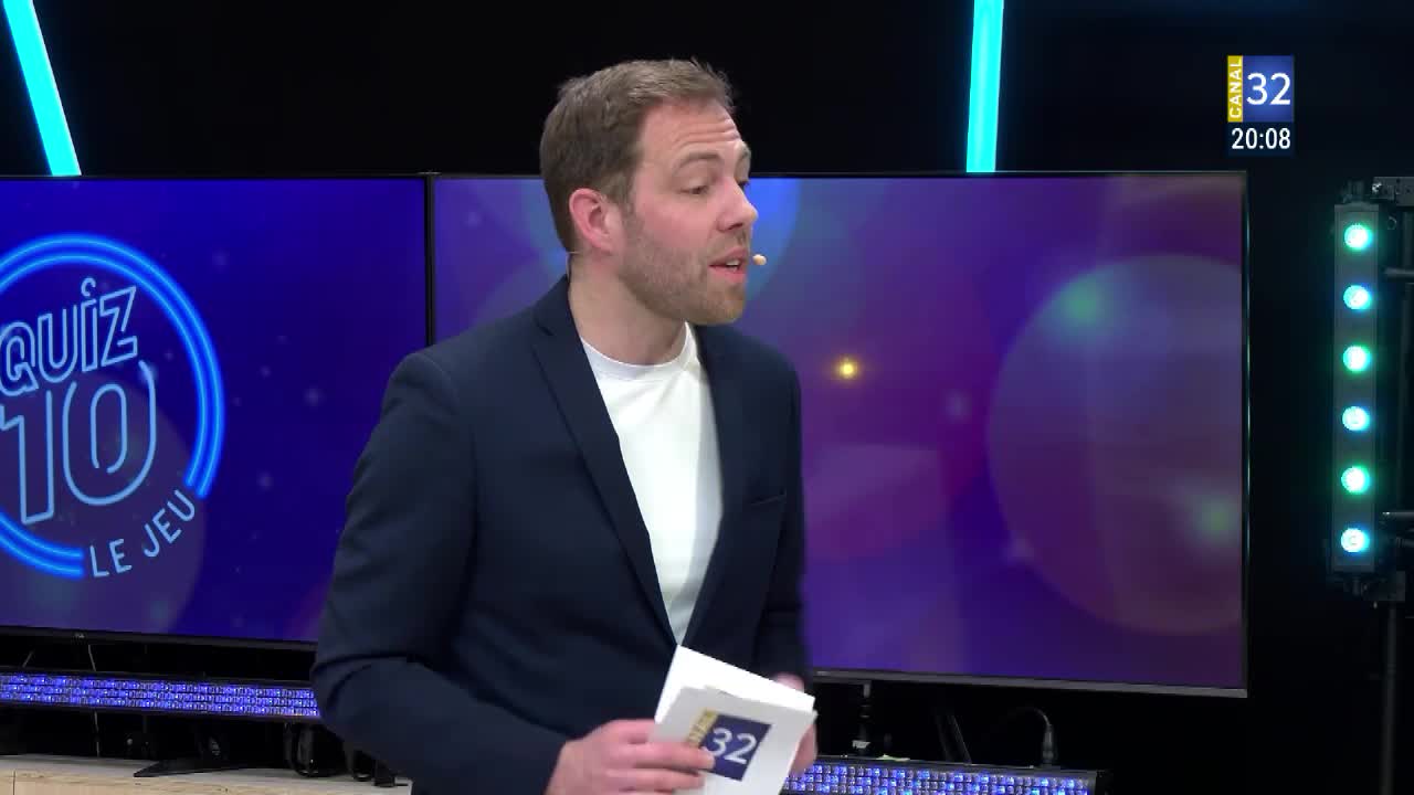 The host, dressed in a navy blazer, is speaking into a microphone, holding a stack of papers. A "Quiz 10" logo glows on the screen behind him, with the Canal 32 logo visible in the corner.
