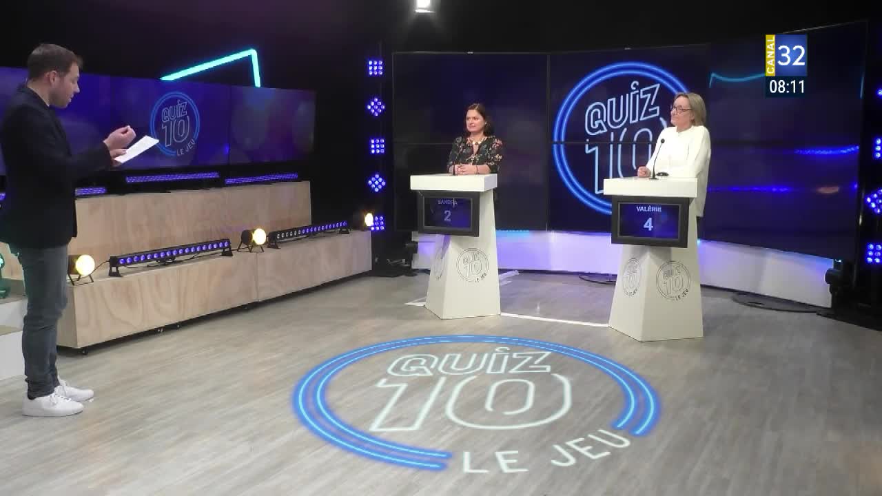 The host, holding a clipboard, stands before two contestants on the set of "Quiz 10" on Canal 32 in France. The contestants, each at a podium, await their next question.
