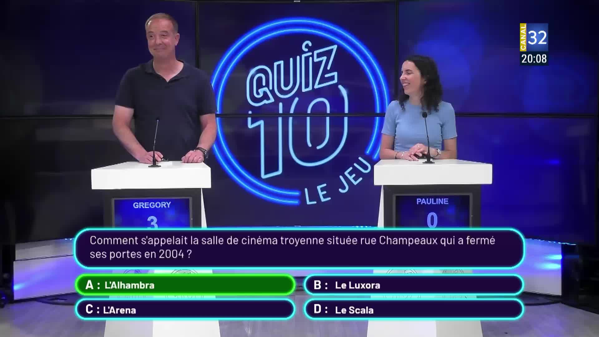 On Canal 32, the French quiz show "Quiz 10 Le Jeu" is underway. Gregory and Pauline stand at their podiums, awaiting the answer to a question about a cinema in Troyes.
