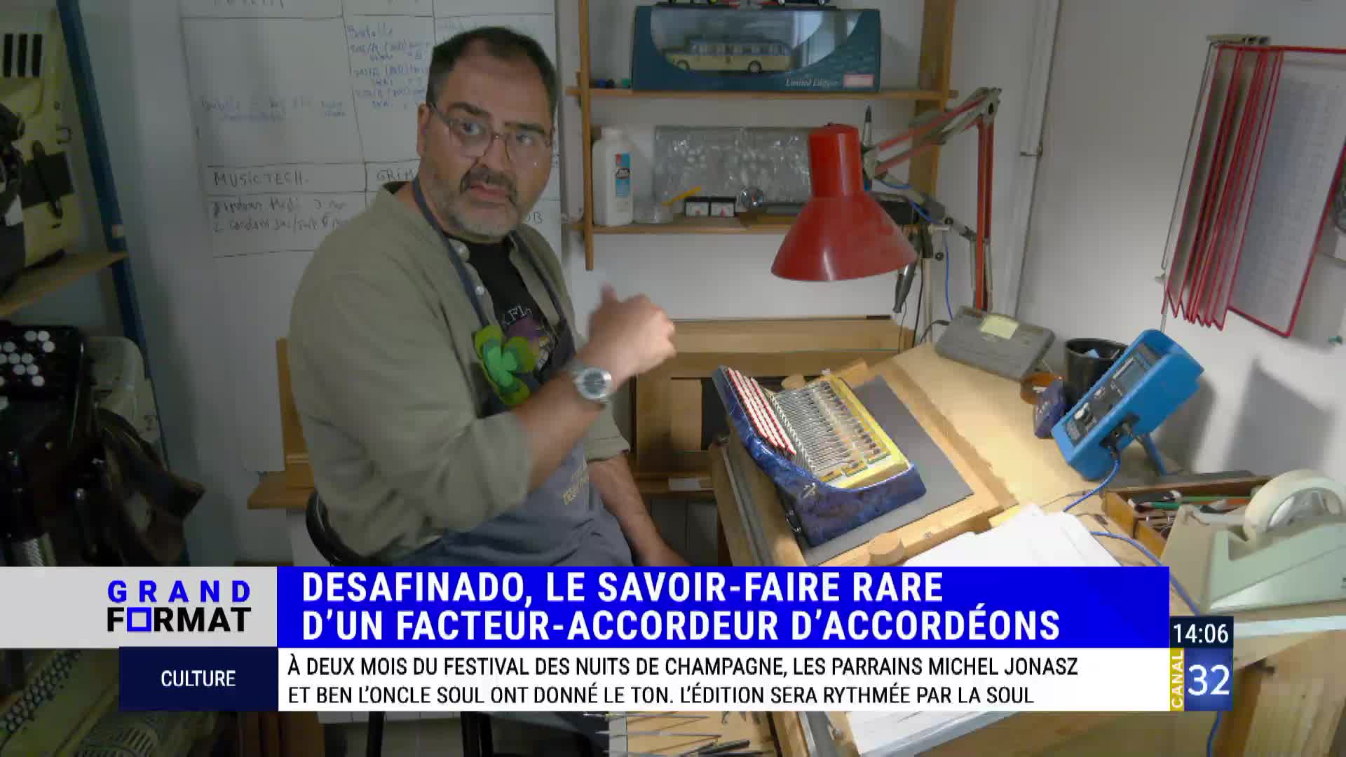 The man, framed by a Canal 32 graphic, gestures with his thumb towards a partially assembled accordion on a workbench. He's in a workshop in France, and the screen's text indicates the segment is about the rare craft of accordion making.
