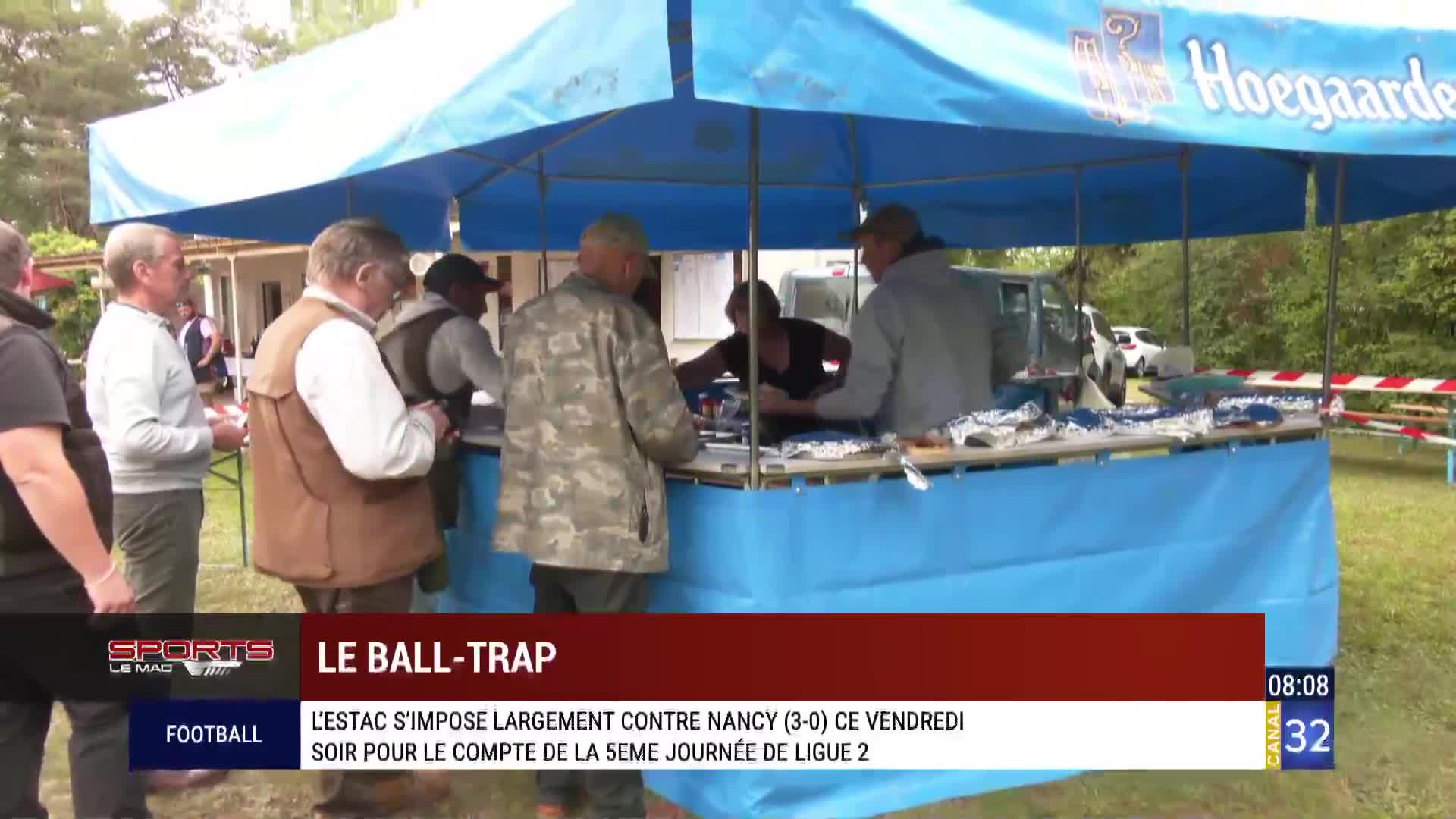 Under a blue canopy, a group of men are gathered, some looking at a table of items. The Canal 32 logo is visible, and the bottom of the screen reports on a football match in France.
