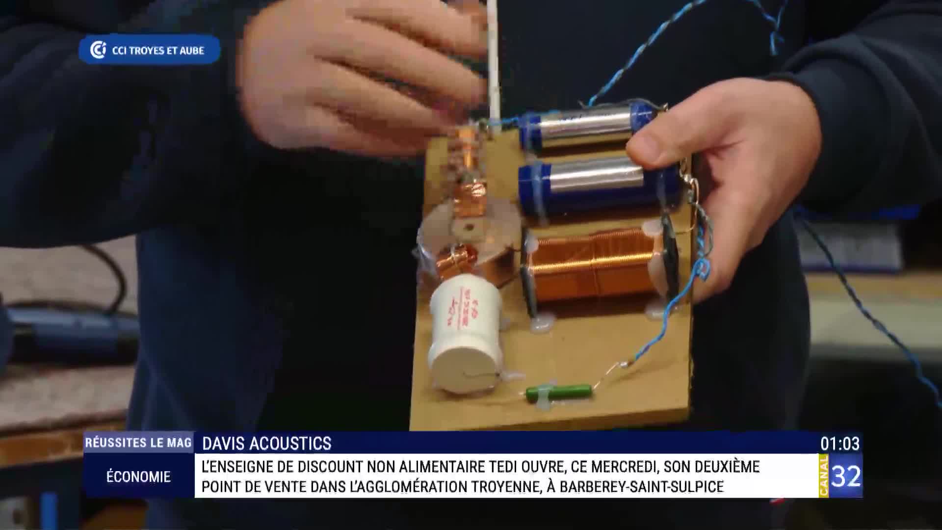 A person holds a circuit board with coils, capacitors, and wires, likely demonstrating something for a segment on Canal 32. The screen shows a story about a new Tedi store opening in Troyes, France.
