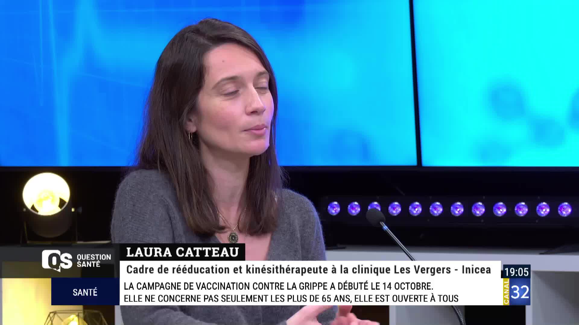 On Canal 32 in France, a woman with dark hair speaks into a microphone, her hands gesturing slightly. The screen behind her is a bright blue, and the lower third displays text about a flu vaccination campaign.
