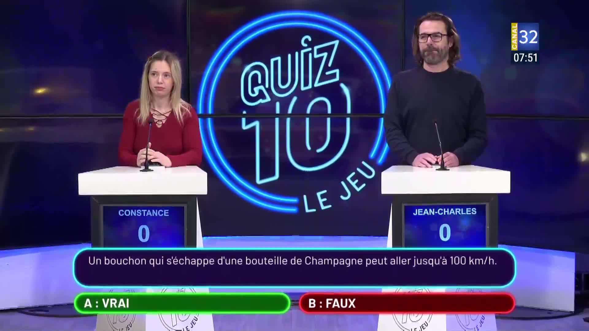 Constance and Jean-Charles stand at their podiums on the set of "Quiz 10 Le Jeu," a broadcast from Canal 32 in France. A question about champagne corks appears on the screen between them.