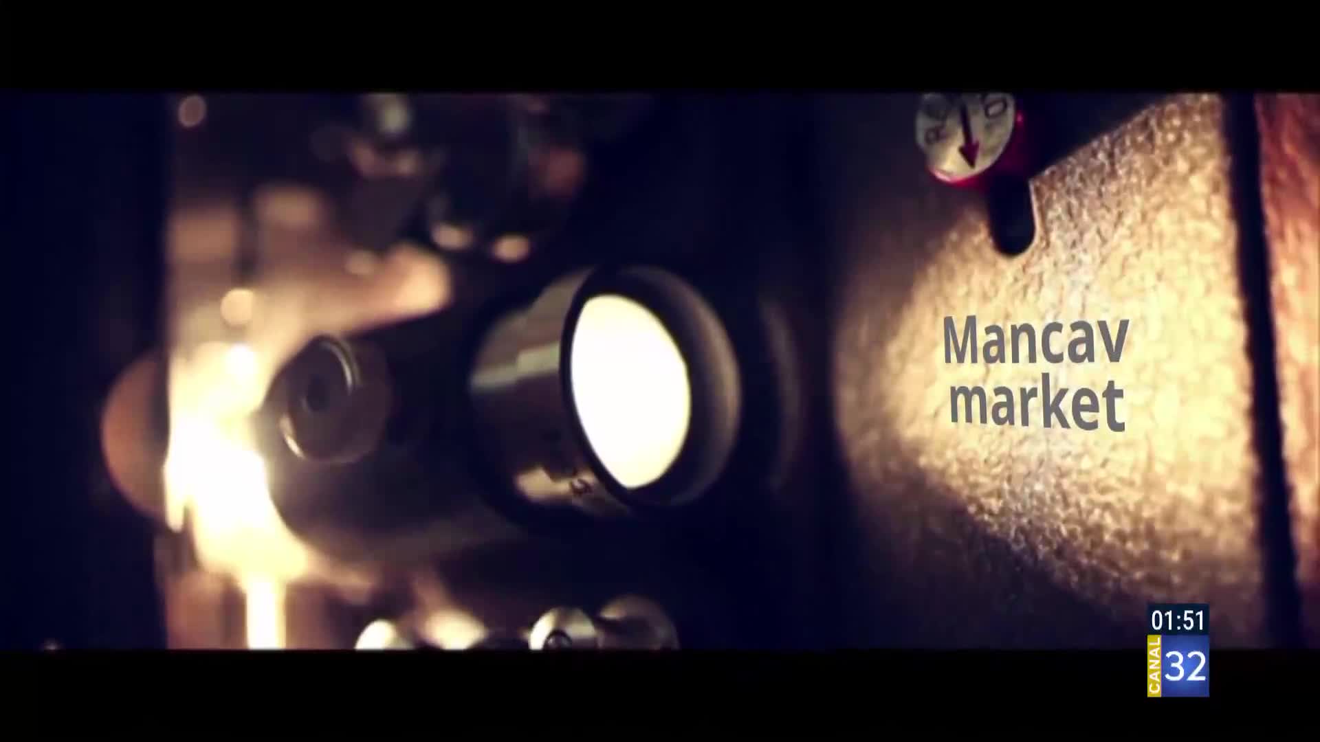 A bright light shines from a projector lens, casting a warm glow on textured metal. Text on the screen reads "Mancav market," with a Canal 32 logo in the corner.