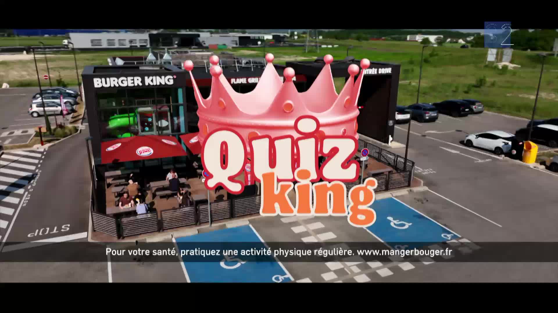 Cars are pulling up to the Burger King drive-thru. A large pink crown with the words "Quiz King" hovers over the building.