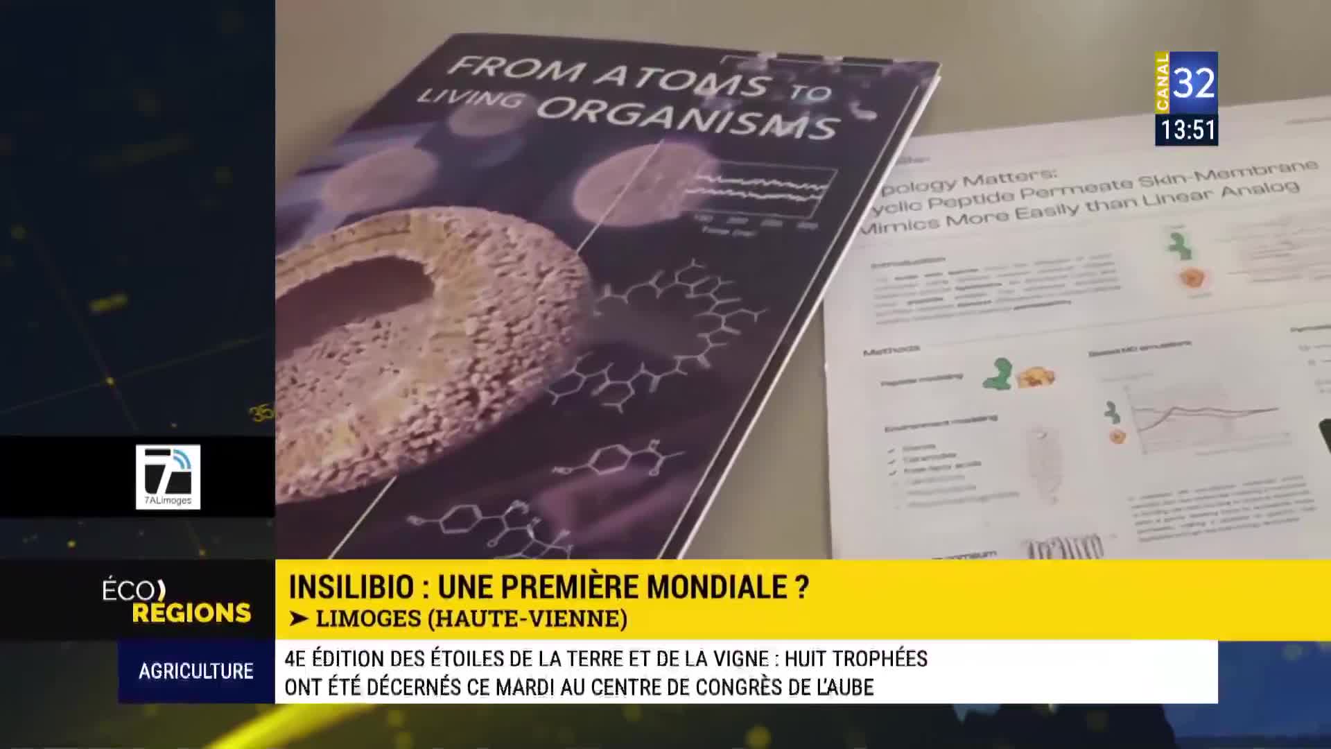 A scientific poster titled "From Atoms to Living Organisms" sits on a table, its molecular diagrams and imagery catching the light. Beside it, another document displays charts and text, hinting at research presented on Canal 32.