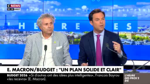 On CNews, two men in suits are discussing Macron's budget plan. The man on the right gestures emphatically as he speaks, while the other listens intently.
