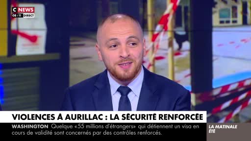 A man in a suit and tie is speaking on CNews, the French television channel. Behind him, a graphic about reinforced security in Aurillac, France, is displayed.
