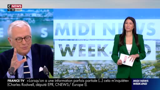 A man in a navy suit gestures emphatically while speaking into a microphone, as seen on CNews. Across the studio, a woman in a green blazer holds a notepad, poised to speak.
