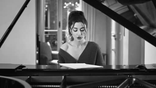 A young woman with her hair pulled up sits at a grand piano, her eyes focused on the sheet music before her. The scene, captured in black and white, suggests a moment of quiet concentration, perhaps for a CNews report or a personal performance in France.
