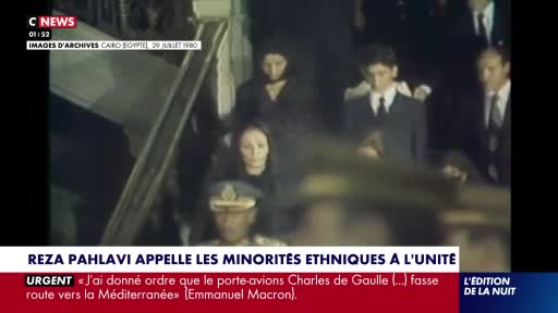 A group of people in formal attire, some in dark suits and ties, ascend a staircase. A woman in a black dress and headscarf is visible in the foreground, her gaze directed forward.