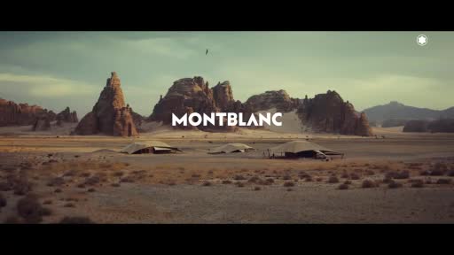 A bird circles above a vast desert landscape dotted with tents. The word "MONTBLANC" appears in large white letters against a backdrop of rugged rock formations. A bird circles above a vast desert landscape dotted with tents. The word "MONTBLANC" appears in large white letters against a backdrop of rugged rock formations.