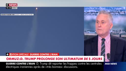 A rocket ascends into the clear blue sky, leaving a thin white plume behind it. A man in a suit and tie speaks into a microphone, his expression serious. A rocket ascends into the clear blue sky, leaving a thin white plume behind it. A man in a suit and tie speaks into a microphone, his expression serious.