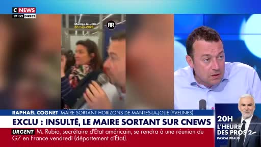 A man is speaking into a microphone, his face close to the lens. A woman with a patterned scarf stands behind him, also looking towards the camera. A man is speaking into a microphone, his face close to the lens. A woman with a patterned scarf stands behind him, also looking towards the camera.