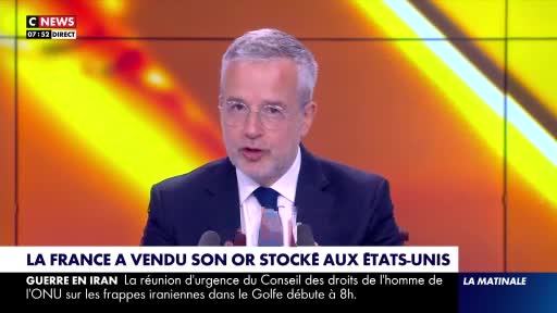 A man in a suit speaks into microphones, his face illuminated by studio lights. Below him, a news ticker scrolls with headlines about France selling gold and a UN meeting on Iran. A man in a suit speaks into microphones, his face illuminated by studio lights. Below him, a news ticker scrolls with headlines about France selling gold and a UN meeting on Iran.