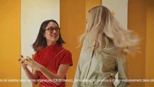 A woman in a red top laughs, holding a yellow object. Her friend, with long blonde hair, turns away, her hair flying out. A woman in a red top laughs, holding a yellow object. Her friend, with long blonde hair, turns away, her hair flying out.