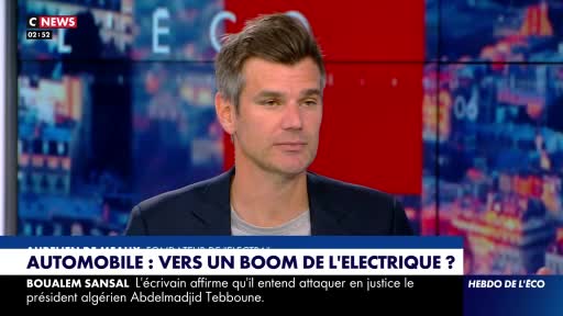 A man with short, graying hair sits in front of a screen displaying C NEWS. Text at the bottom of the screen reads "AUTOMOBILE : VERS UN BOOM DE L'ELECTRIQUE ?" A man with short, graying hair sits in front of a screen displaying C NEWS. Text at the bottom of the screen reads "AUTOMOBILE : VERS UN BOOM DE L'ELECTRIQUE ?"
