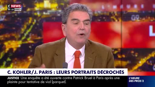 A man in a brown jacket and orange tie speaks animatedly on C News. The screen behind him displays a cityscape at night. A man in a brown jacket and orange tie speaks animatedly on C News. The screen behind him displays a cityscape at night.