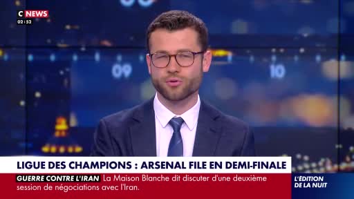 A man in a suit and tie speaks directly to the camera, his glasses reflecting the studio lights. Below him, a news ticker scrolls with headlines about the Champions League and Iran.