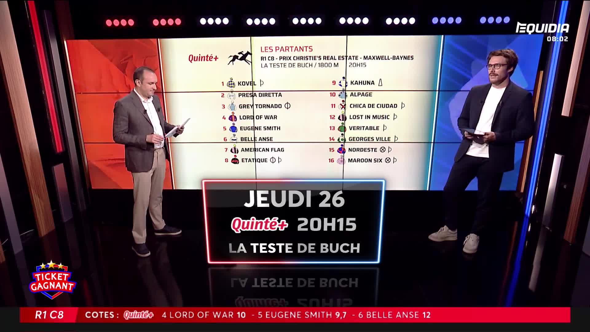 Two men in suits stand in a studio, discussing the upcoming Quinté+ race at La Teste de Buch. One holds papers, while the other gestures towards a screen displaying the race details on Equidia.
