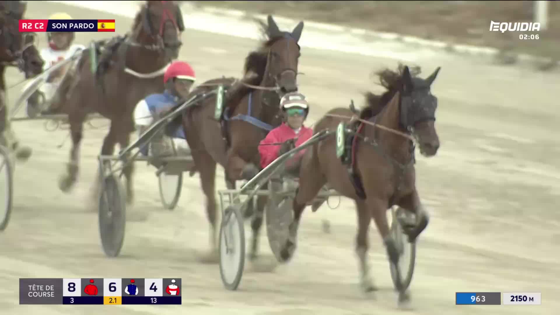 The horses, each pulling a sulky, are thundering down the track. The drivers, wearing helmets and colorful jackets, urge their steeds forward.

