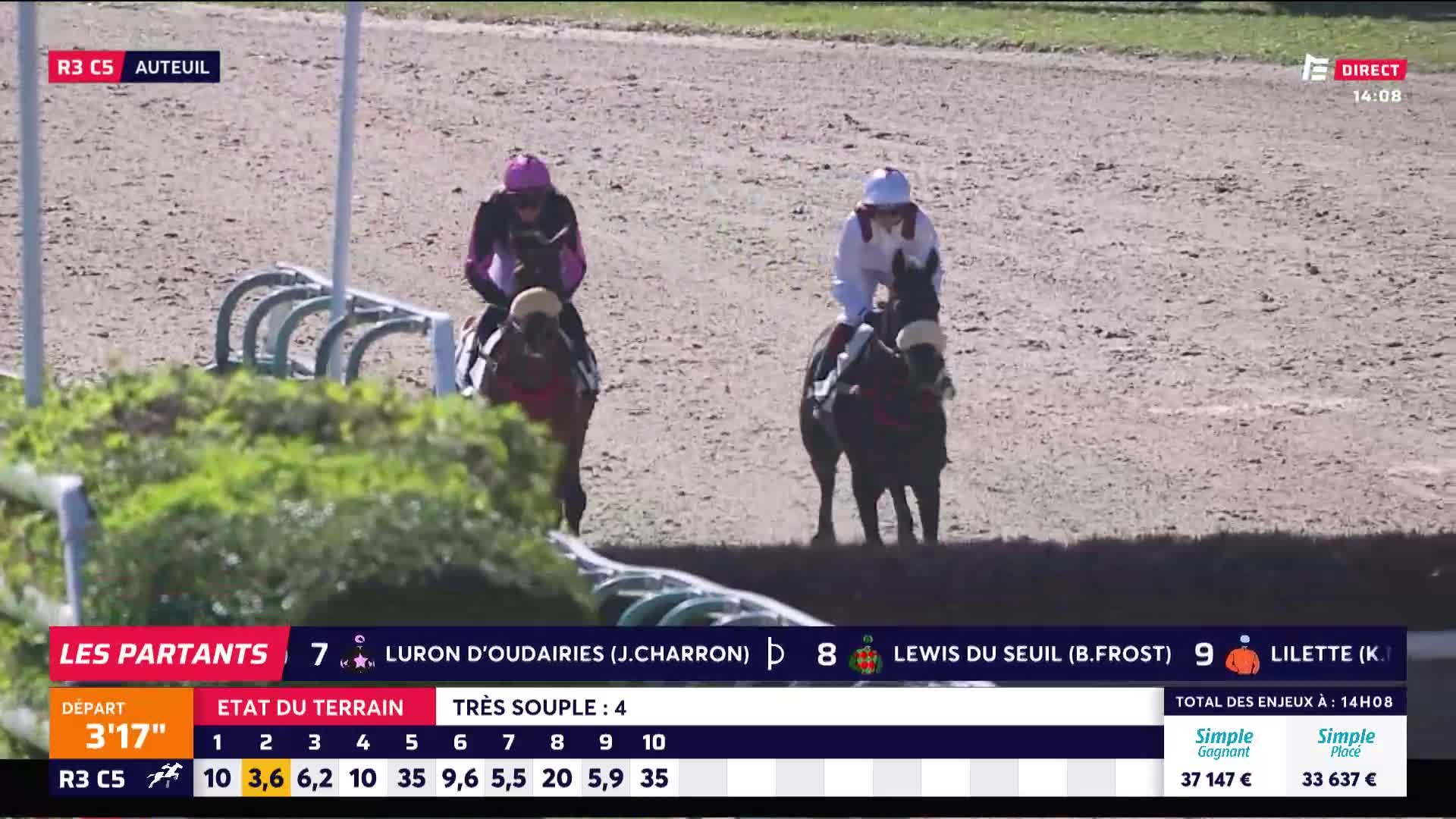 Two horses, each ridden by a jockey in silks, approach a low hedge. The horses are on the track at Auteuil, part of a race broadcast by Equidia.
